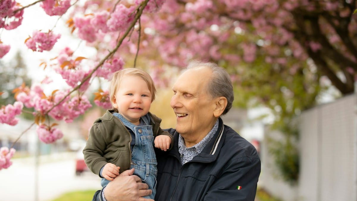 Grandfather holding his smiling grandson under a blossoming tree